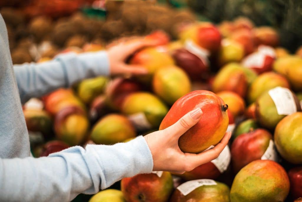 Frau hält eine Mango im Supermarkt