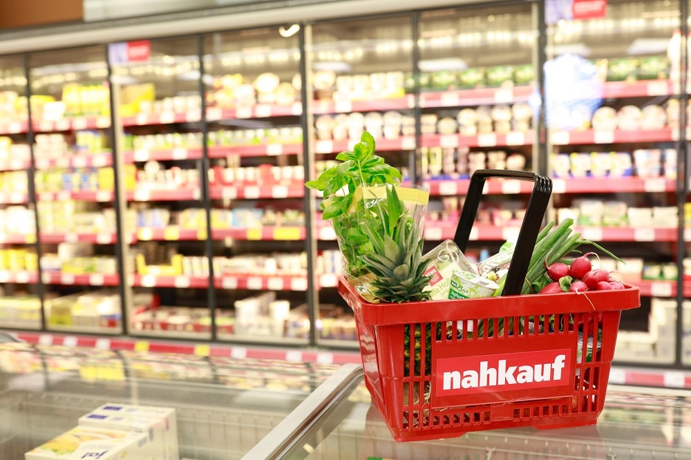 nahkauf Einkaufskorb in einer Filiale. Der Korb steht mit Obst gefüllt vor einem Kühlregal und auf einer Gefriertruhe