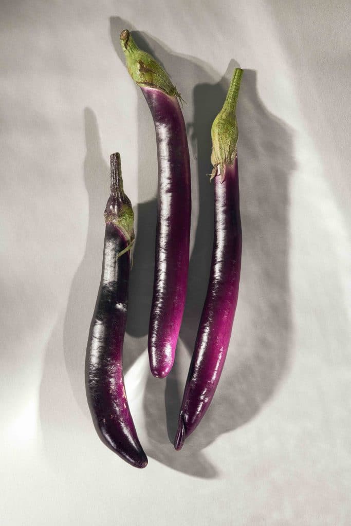 Drei Mini-Auberginen liegen auf einer grauen Fläche
