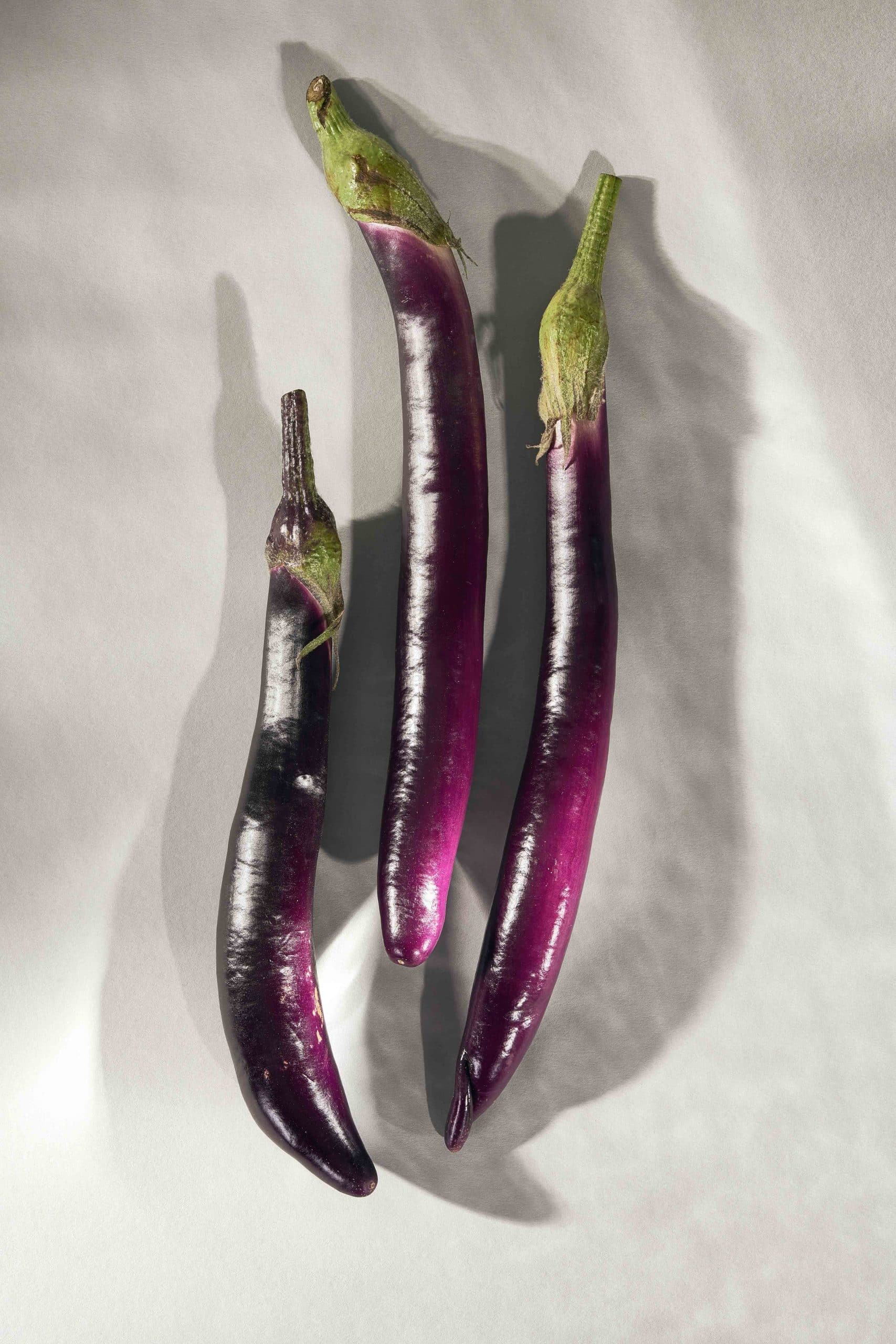 Drei Mini-Auberginen liegen auf einer grauen Fläche