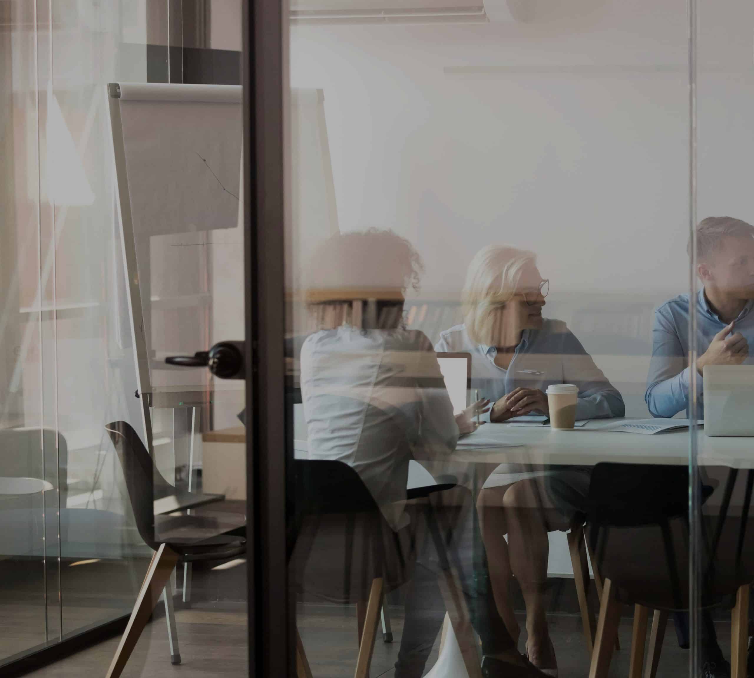 Zwei Frauen und ein Mann sitzen in einem Besprechungsraum mit Laptops und Kaffee
