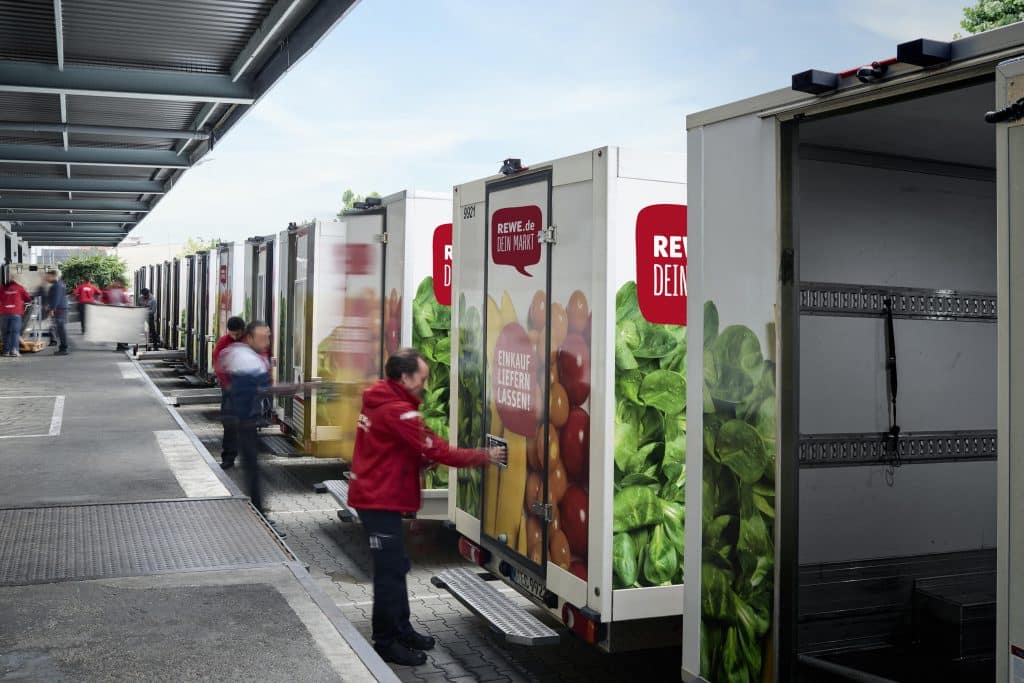 Eine Gruppe von REWE-Mitarbeitenden entladen LKWs