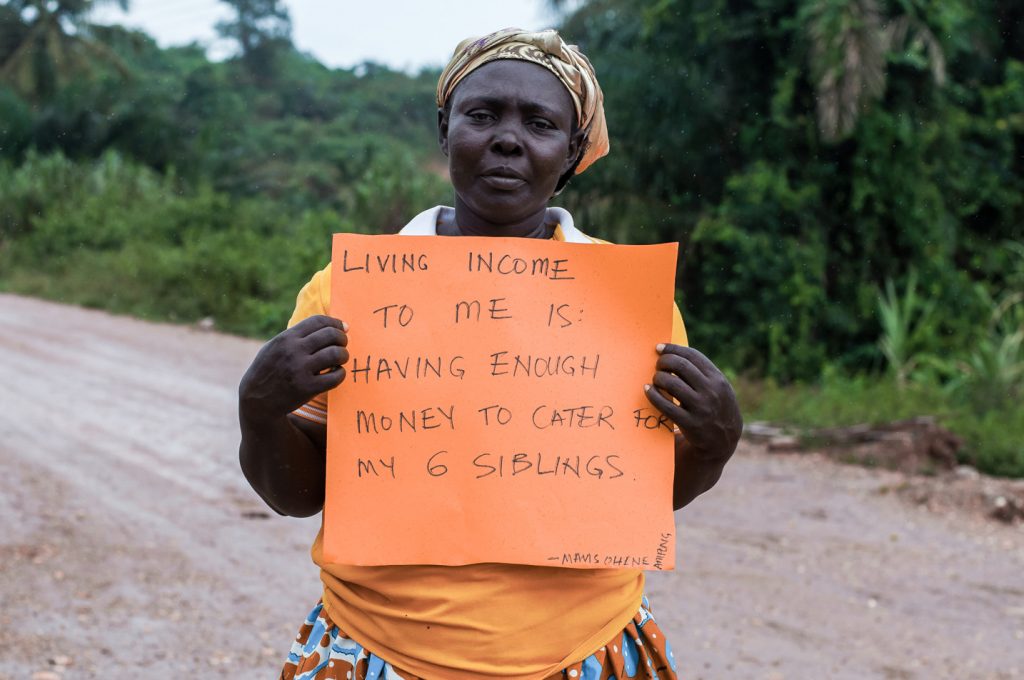 Eine Farmerin hält ein Schild hoch, auf dem geschrieben steht: „Existenzsichernder Lohn bedeutet für mich, genug Geld zu haben, um meine sechs Geschwister zu unterstützen.“