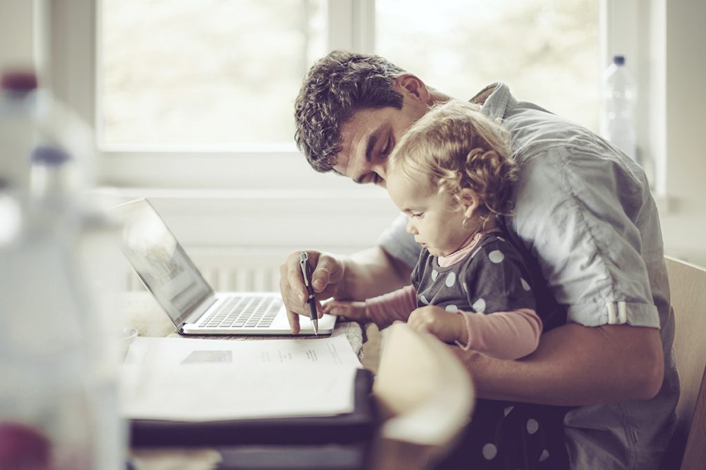 Ein Kind sitzt auf dem Schoß des Vaters und schaut ihm bei der Arbeit zu.