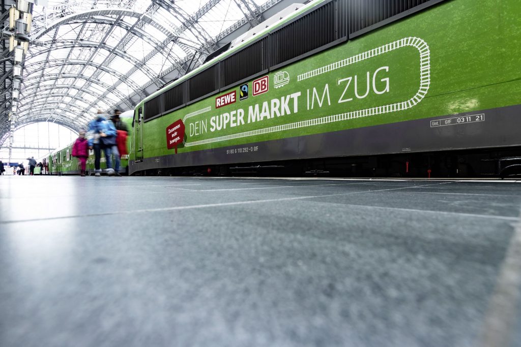 Der REWE Supermarktzug steht auf den Gleisen im Bahnhof