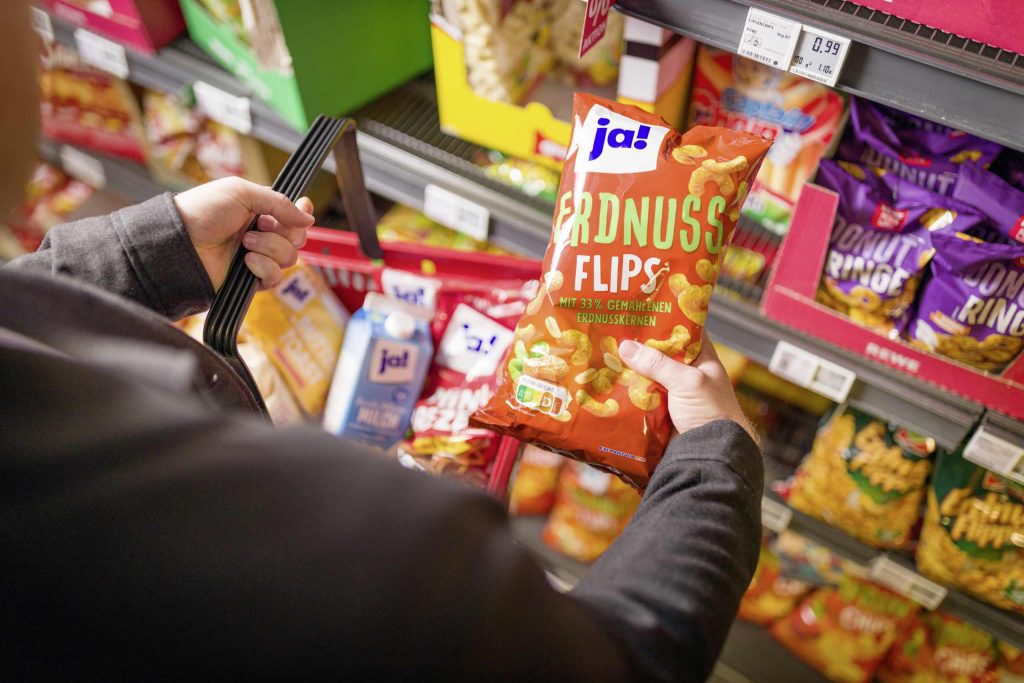 Ein Kunde hält im Supermarkt eine Packung Ja! Erdnussflips