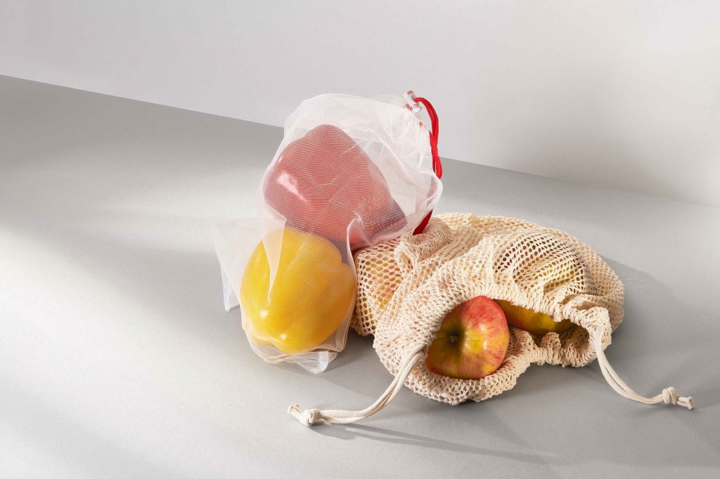 Zwei Mehrwegfrischenetze auf einer weißen Fläche. Eines mit Paprika und eines mit Äpfeln.