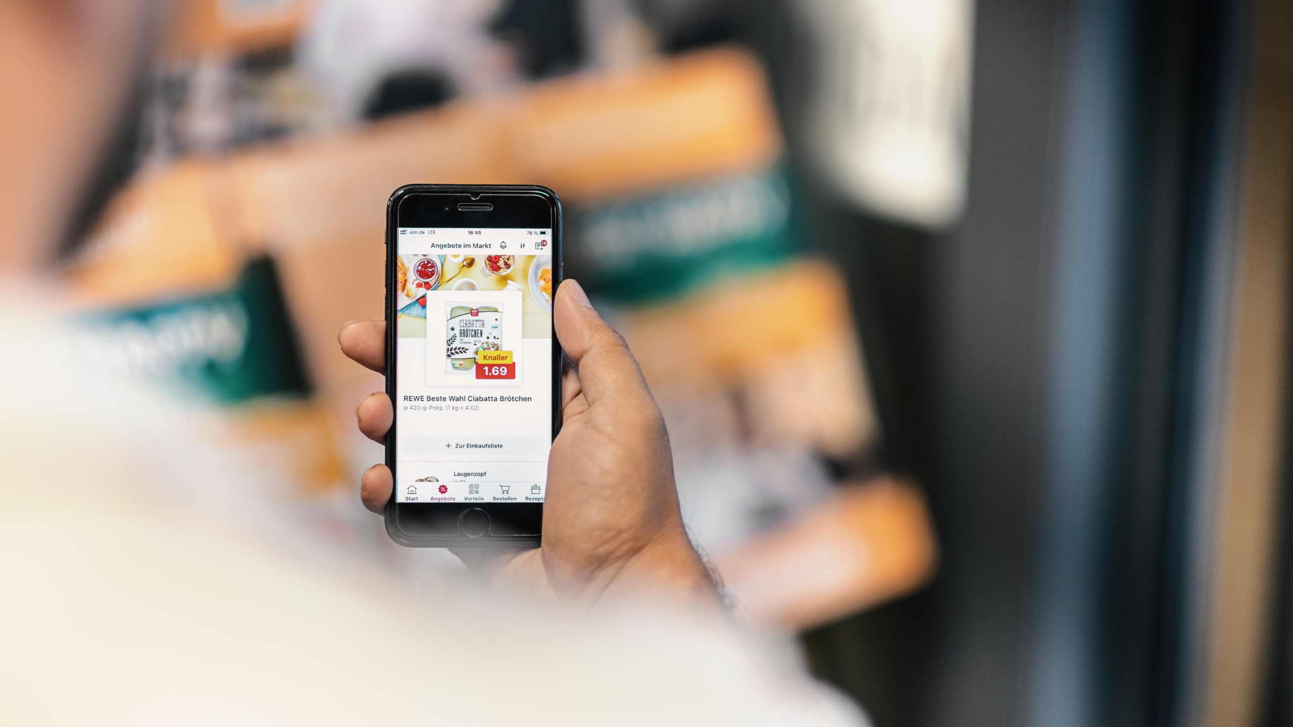 Hand mit geöffneten Angeboten von REWE auf einem Smartphone.