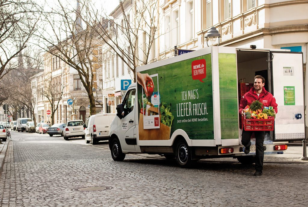 Ein REWE-Mitarbeiter liefert bestelle Ware an Kunden aus.