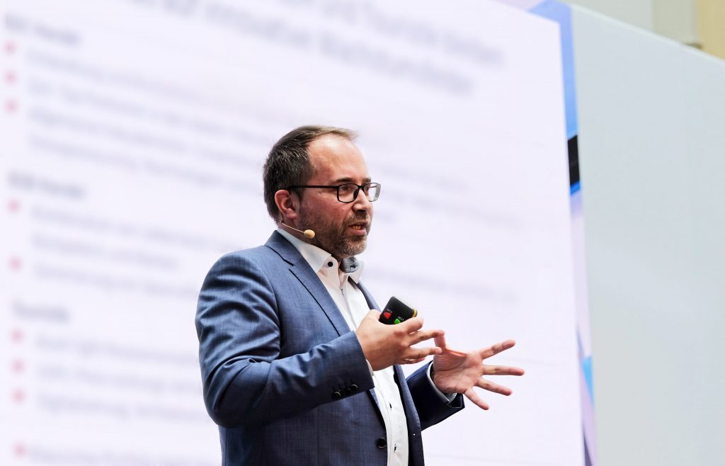 Telerik Schischmanow steht mit Mikrofon auf einer Bühne und hält einen Vortrag