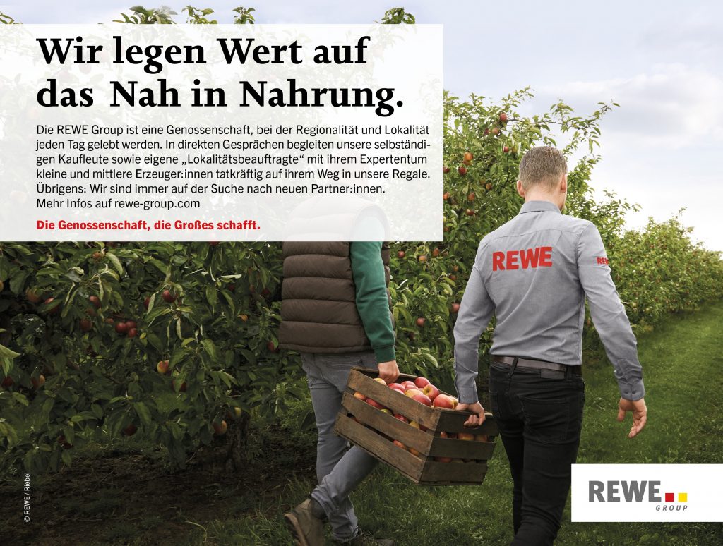 Zwei Menschen tragen eine Kiste mit Äpfeln durch ein Apfelfeld.