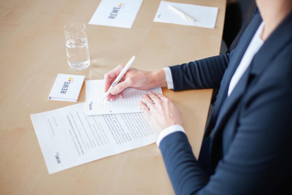 Frau mit REWE Group Stift in der Hand schreibt auf einem Notizblock.