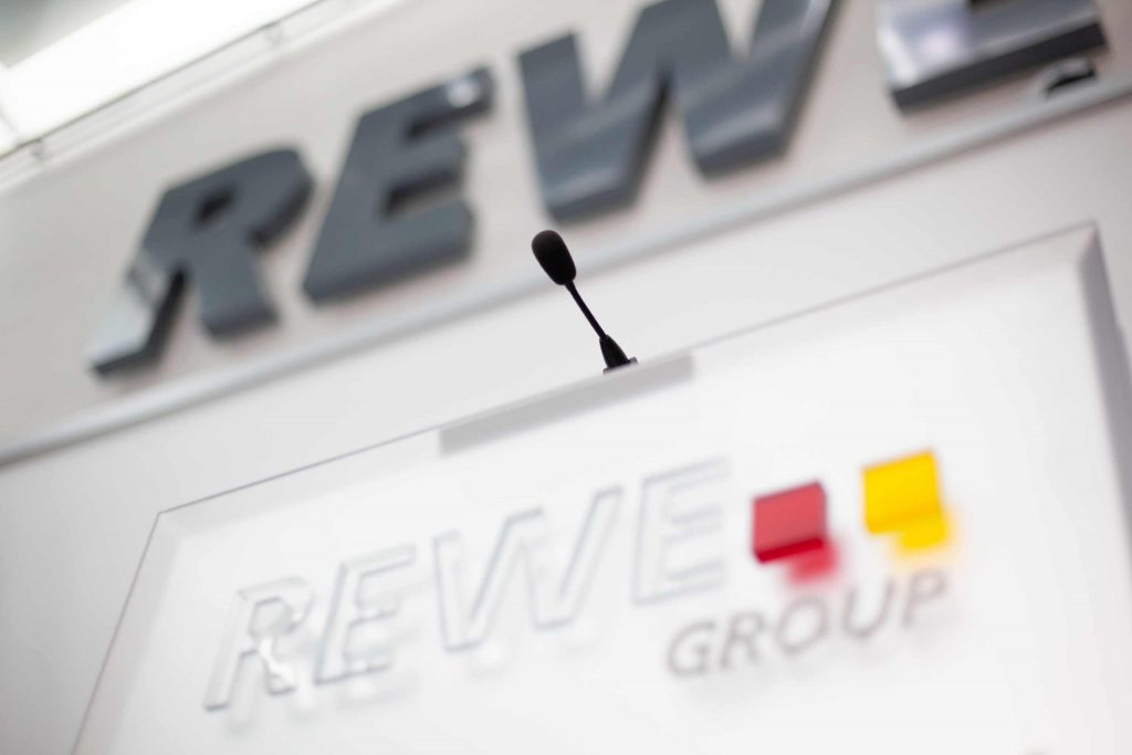 Verschwommenes Rednerpult mit REWE Group Logo