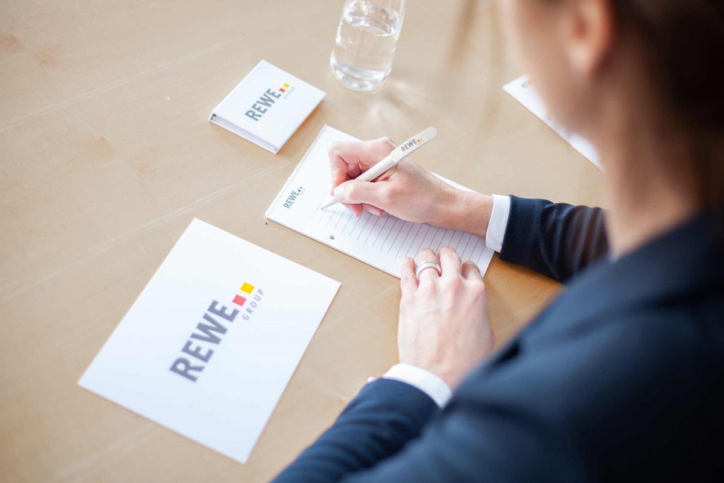 Frau mit REWE Group Stift in der Hand schreibt auf einem Notizblock.