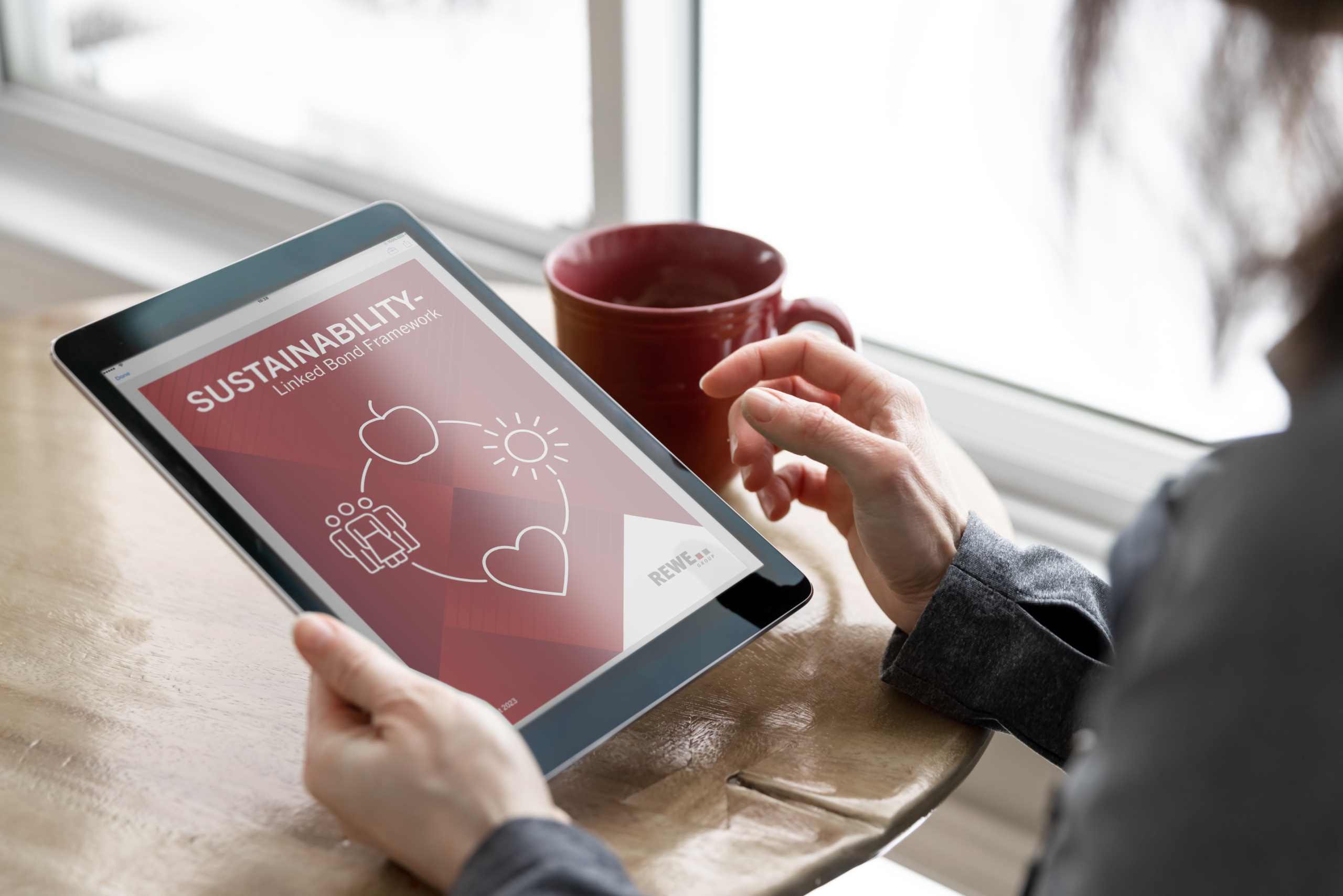 Person mit Tablet die eine Broschüre zum Thema Sustainability-Linked Bond Framework geöffnet hat.