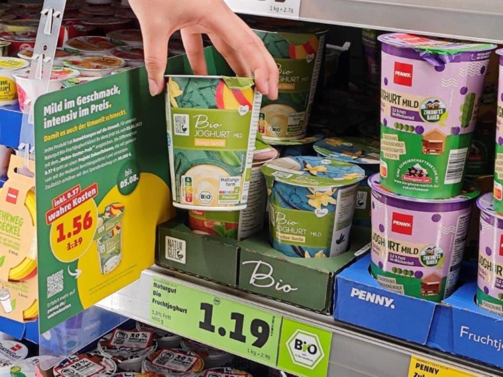 Hand mit Jogurt vor Regal