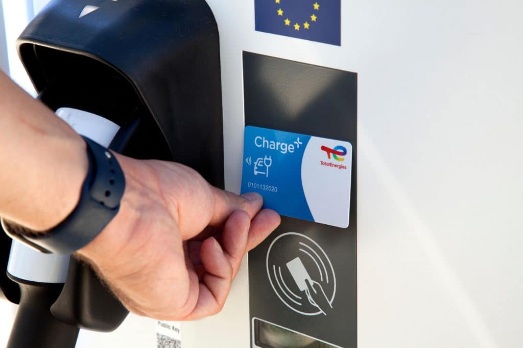 Hand mit Ladekarte von TotalEnergies an E-Ladessäule.