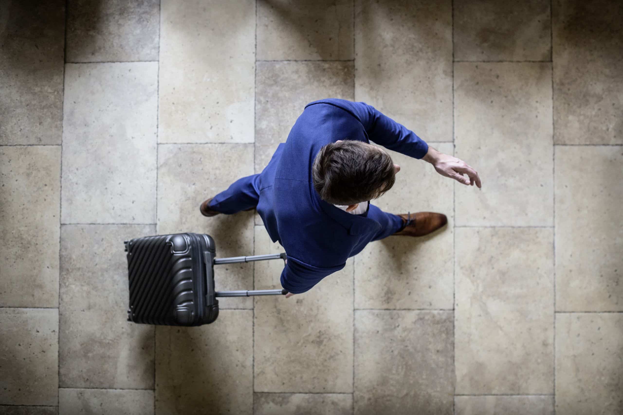 Person von oben, die mit einem Koffer in der Hand nach vorne geht.