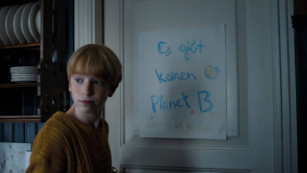 Kind vor einem mit Buntstiften gemalten Blattpapier auf dem 