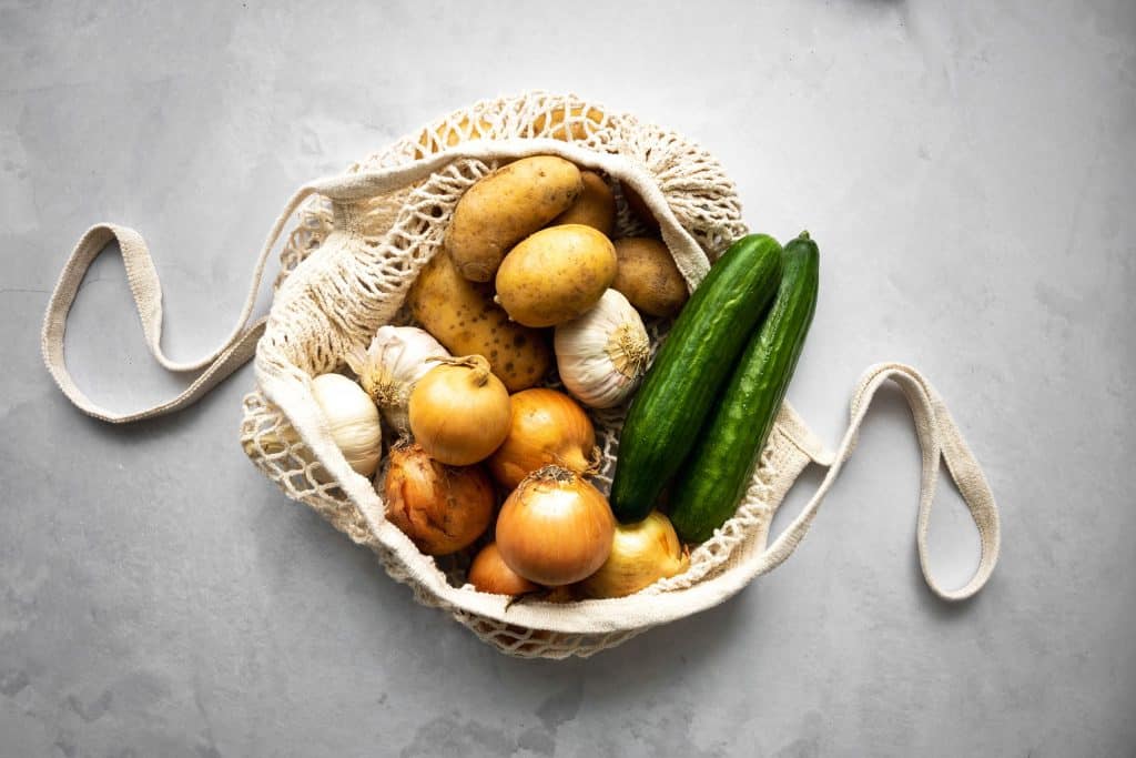 Einkaufsnetz von oben mit Kartoffeln, Gurken, Zwiebel und Knoblauch